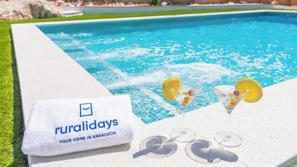 Un espace piscine avec une serviette sur laquelle est inscrit « Ruralidays, votre chez-vous en Andalousie », ainsi que deux verres à martini garnis de tranches de citron.