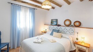 Une chambre à coucher bien rangée, avec un lit, des tables de chevet, une commode, une fenêtre avec des rideaux et des éléments décoratifs sur les murs.