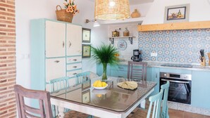 Une cuisine équipée d’une table à manger, de chaises, d’un panier de fleurs, d’une machine à café et d’une cuisinière.