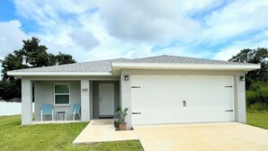 Une maison de plain-pied avec un garage, une véranda à l’avant dotée de deux chaises et un petit jardin.