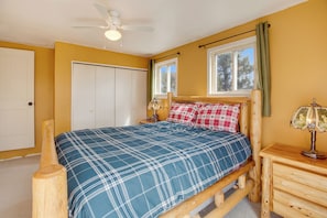 Une chambre à coucher avec un lit en bois, un ventilateur de plafond, une table de chevet avec une lampe et une fenêtre avec des rideaux.