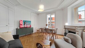 A modern living room with a herringbone floor, a television, a fireplace, and a dining area with a view of the city. - Amazing refurbished flat in Paris V (Paris)