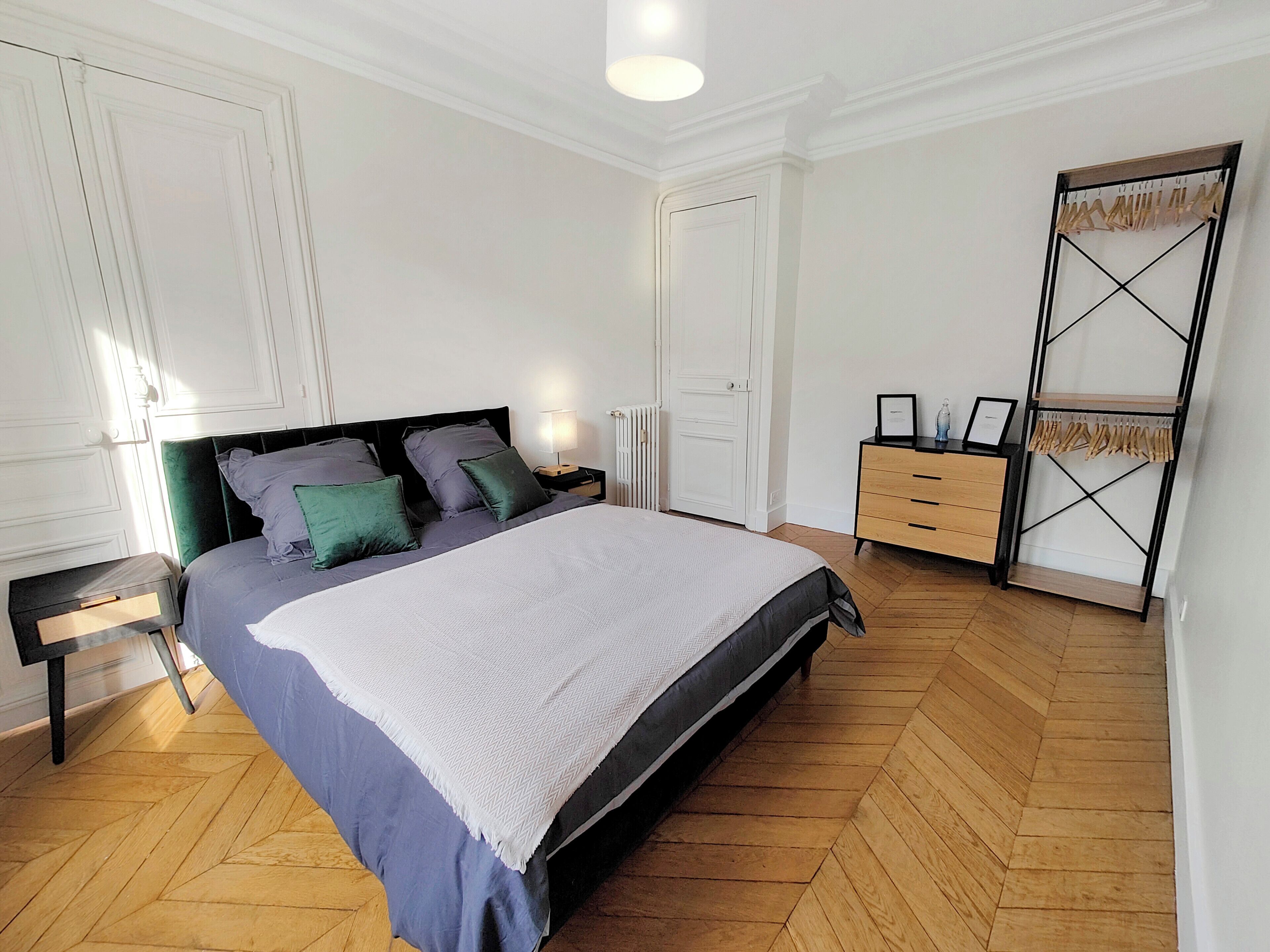 Une chambre à coucher comprenant un lit, une table de chevet, une commode et un portant à vêtements.