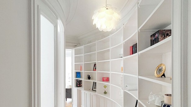 A hallway with a white wall, a wooden floor, and a white shelving unit with various items on it. - Amazing refurbished flat in Paris V (Paris)