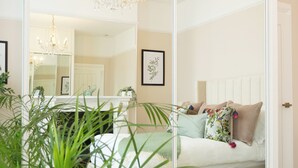 A bedroom with a large mirror, a bed with floral pillows, a chandelier, and a potted plant. - Luxury Victorian Home London (London)