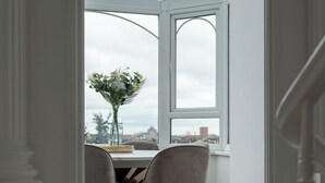 A dining area with a table and chairs, a vase of flowers, and a view through a large window. - Luxury Victorian Home London (London)