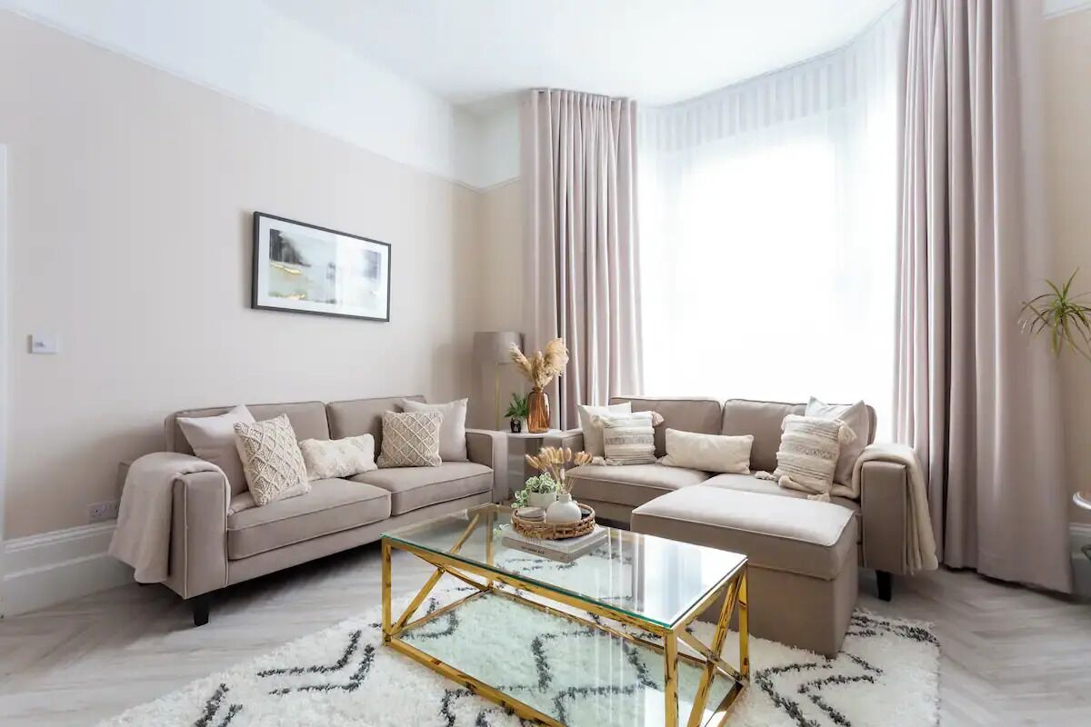 Una sala de estar moderna con un sofá color beige, una mesa de centro de vidrio y un tapete mullido blanco.