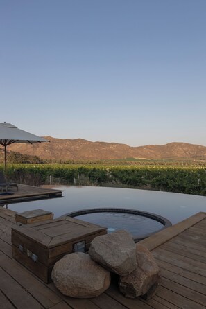 A wooden deck with a hot tub, lounge chairs, and a view of a vineyard and mountains.