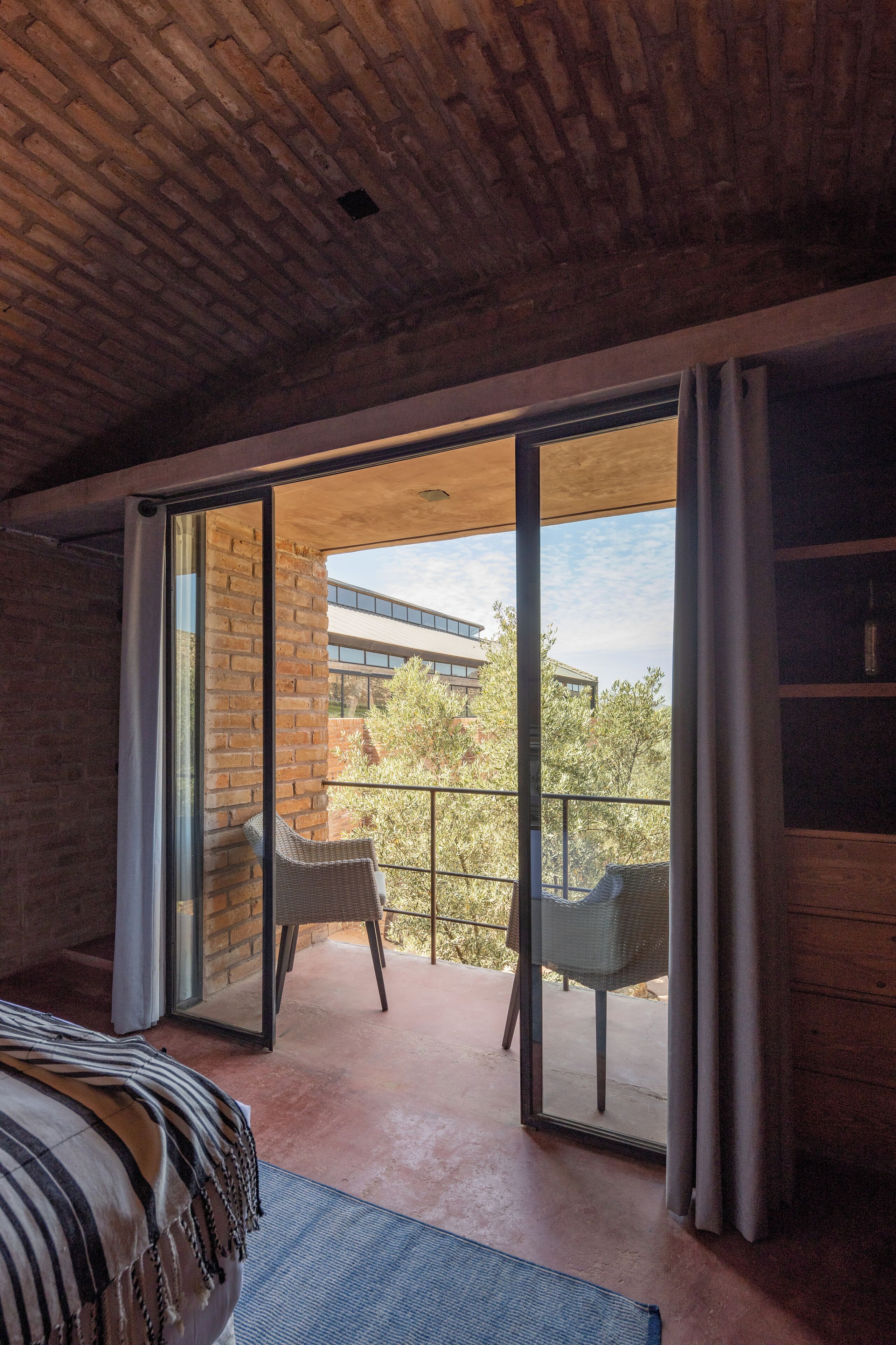 A modern room with a brick ceiling, large sliding glass doors leading to a balcony, and a wicker chair on the balcony.