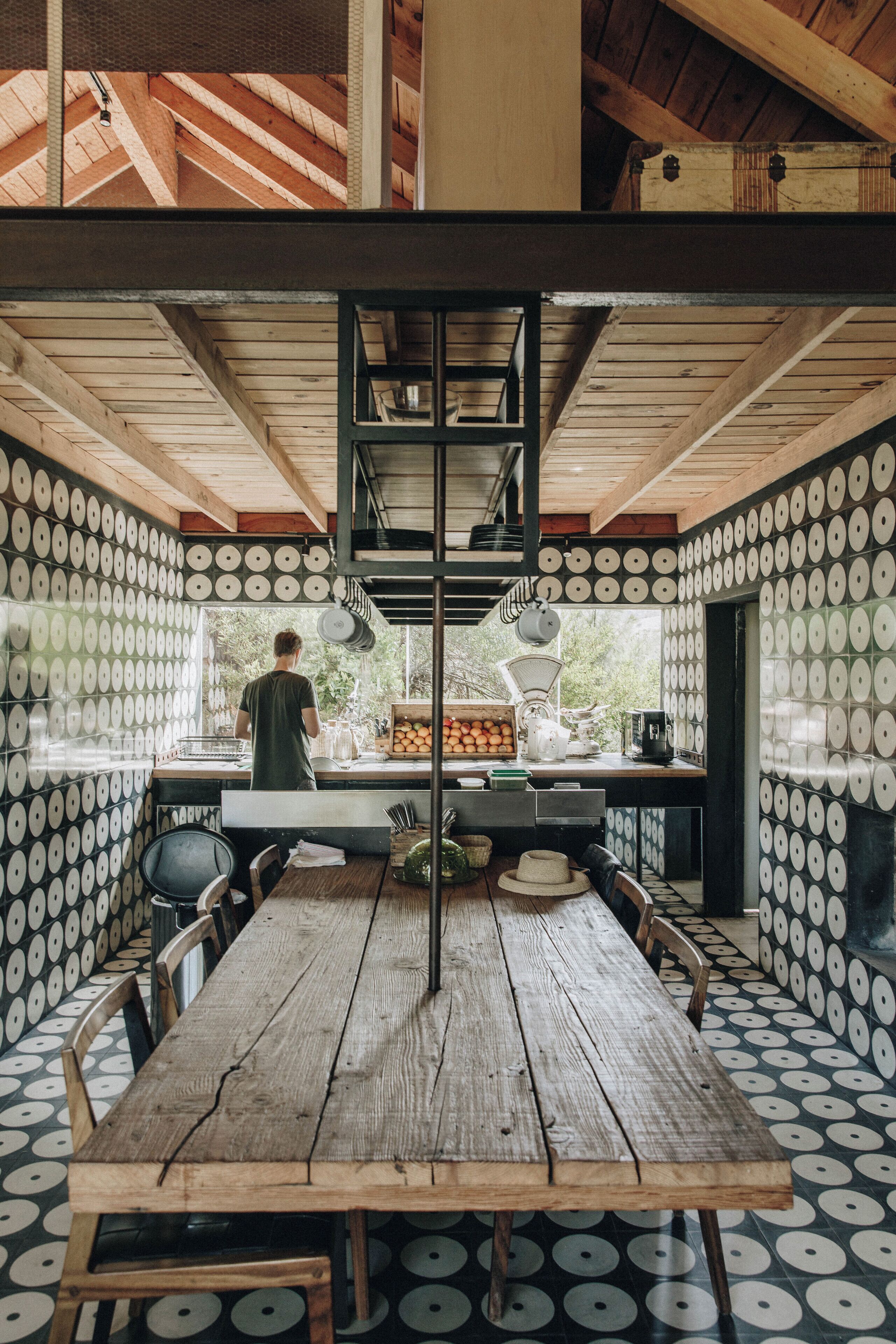 Una mesa de madera rústica con un soporte metálico central en una habitación con paredes de diseño.