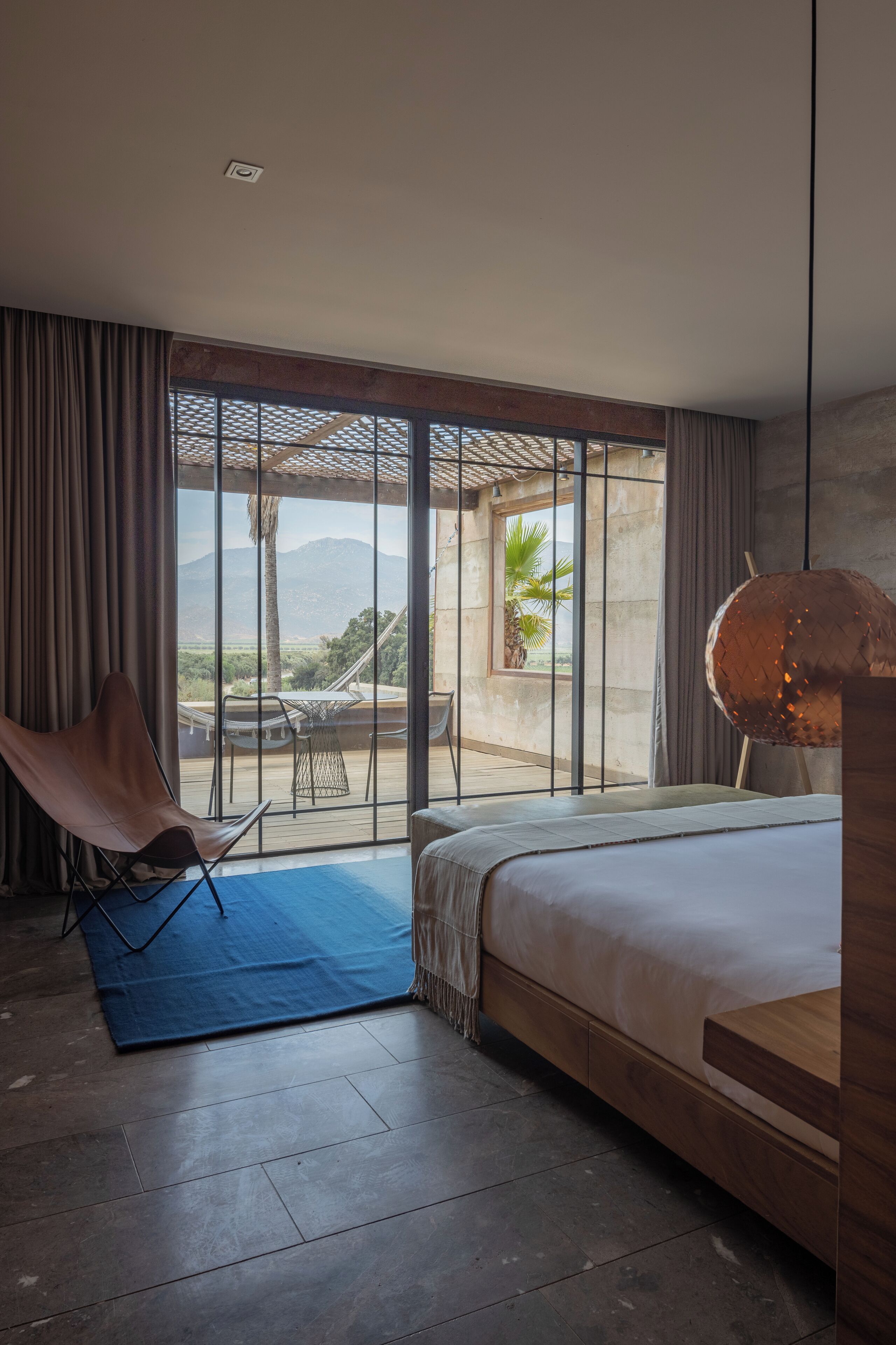 A bedroom with a large bed, a chair, a table, and a view of the outdoors.