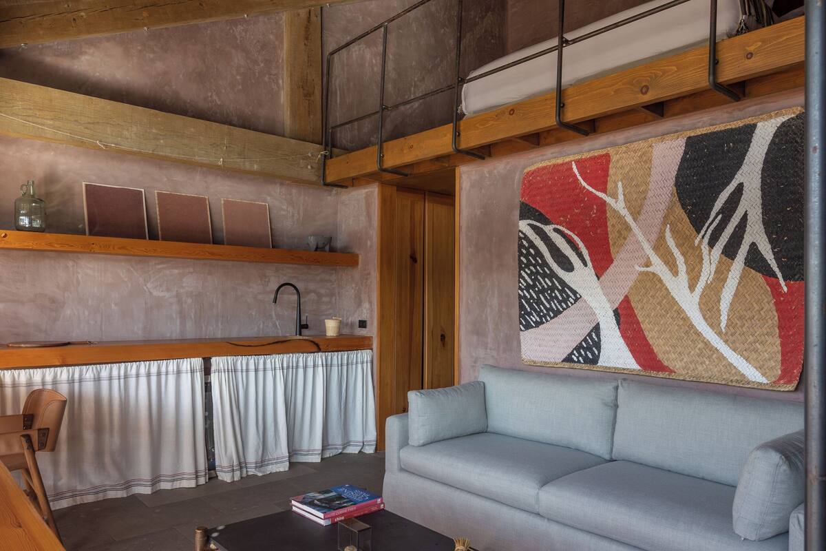 A cozy living room with a wooden ceiling, a sofa, a coffee table, and a wall-mounted shelf with decorative items.