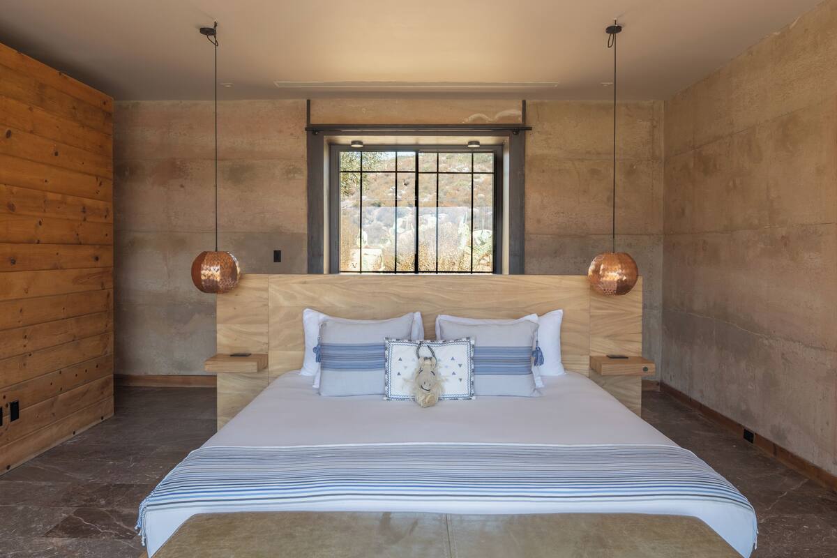 A bedroom with a large bed, wooden walls, a window with bars, and two pendant lights.