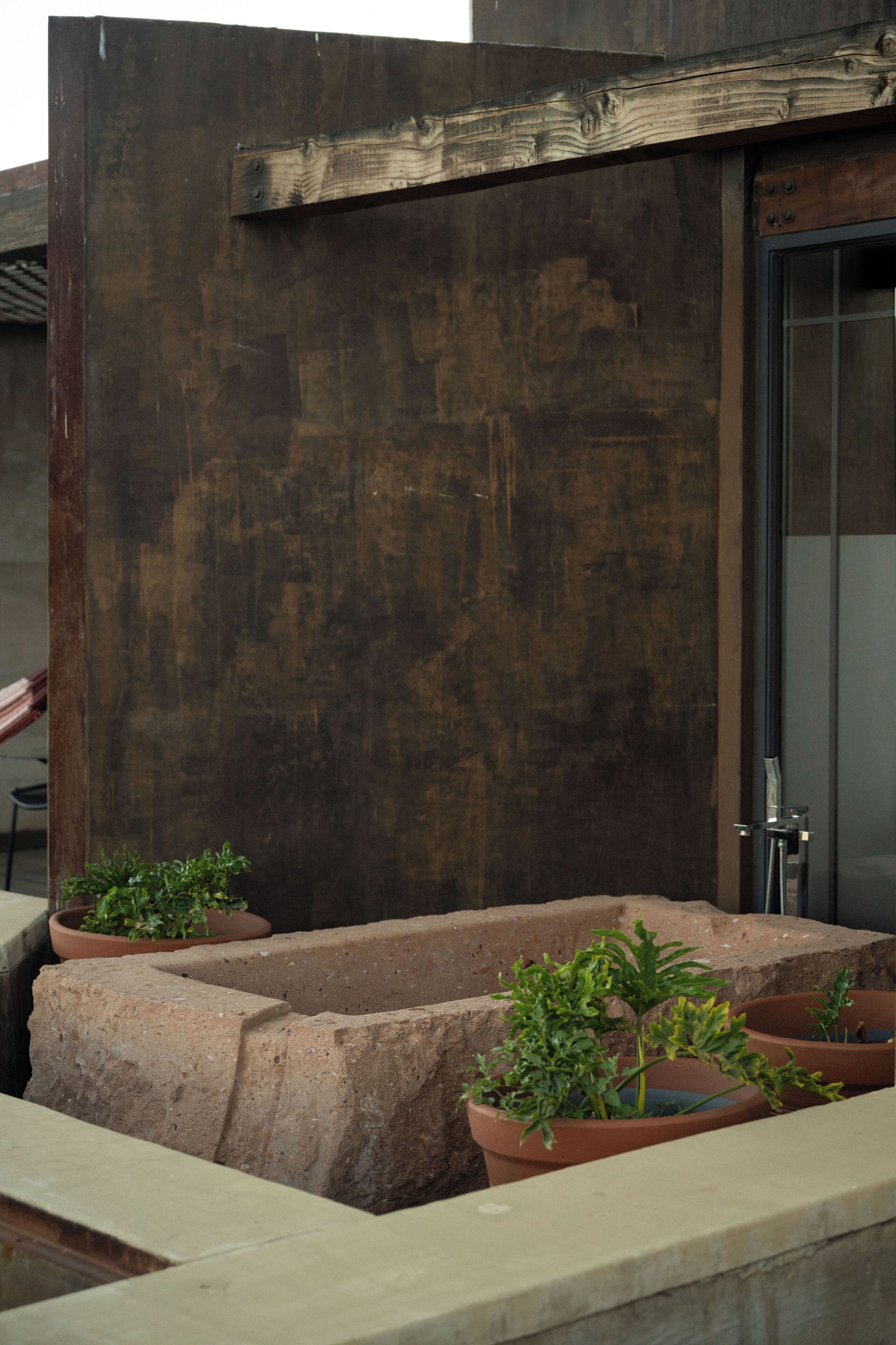 A concrete planter with a potted plant, a wooden beam, and a glass door.