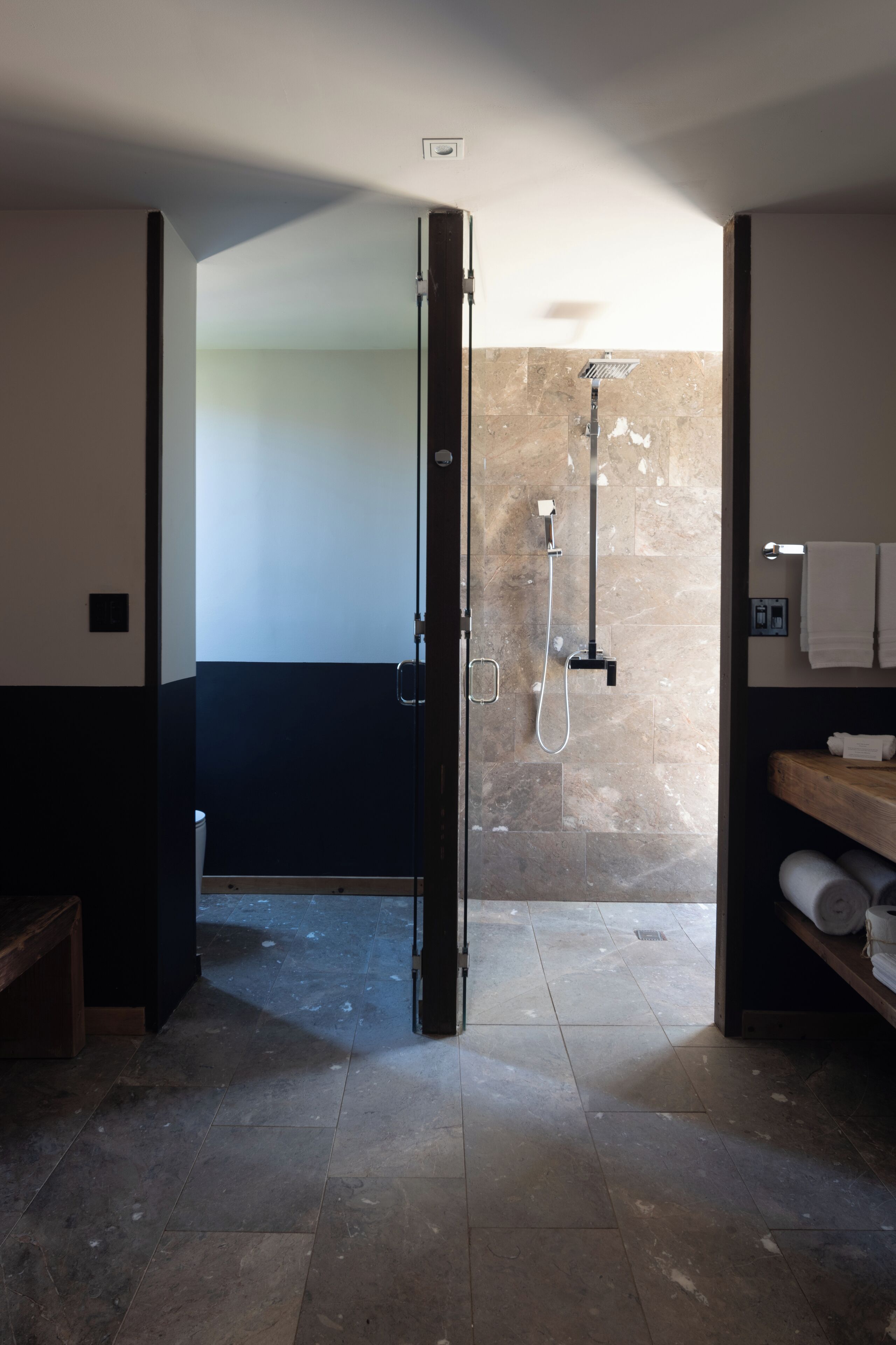 A modern bathroom with a glass-enclosed shower, a wooden bench, and a towel rack.