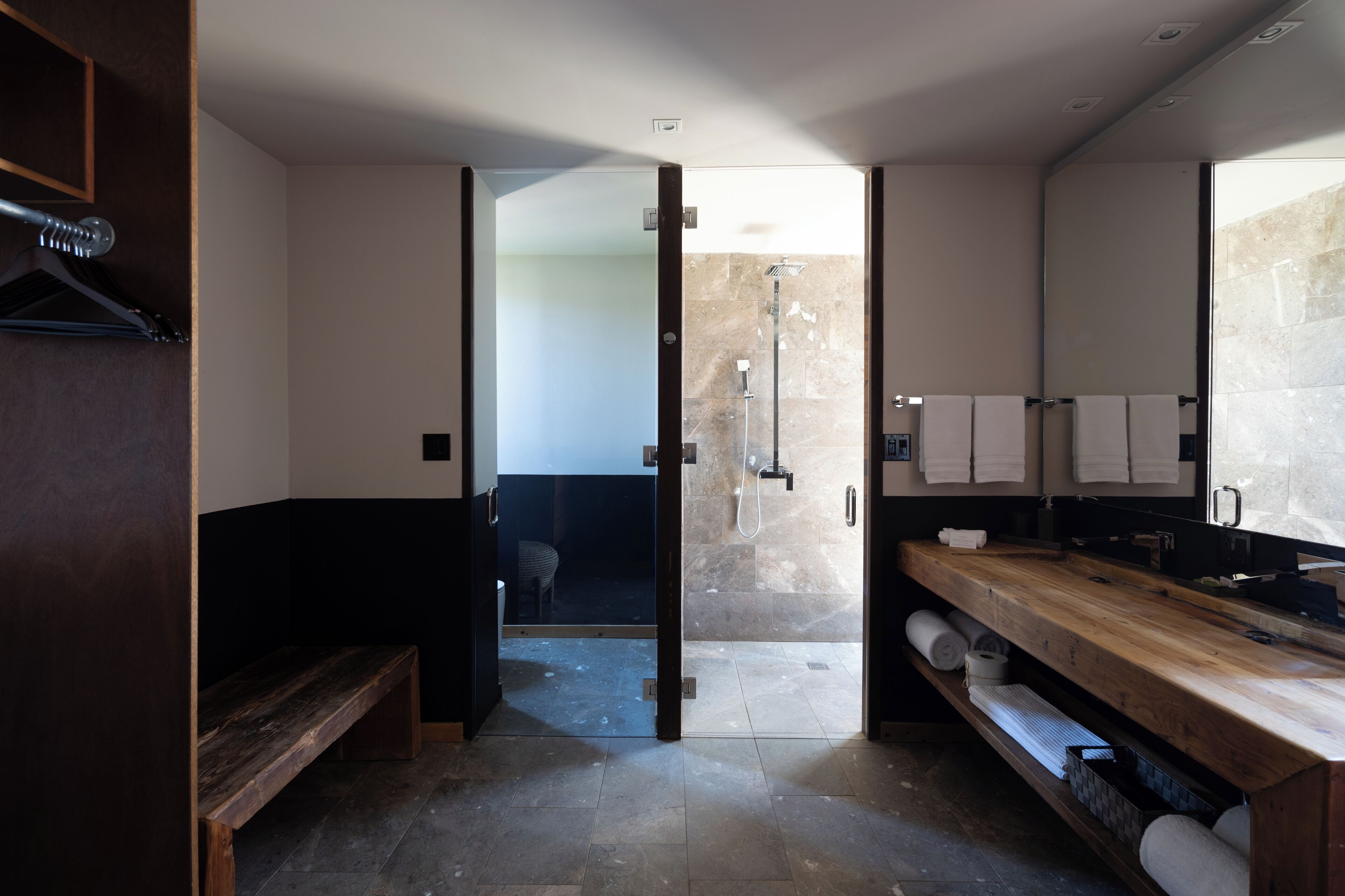 A modern bathroom with a wooden bench, a shower area, and a vanity with towels.