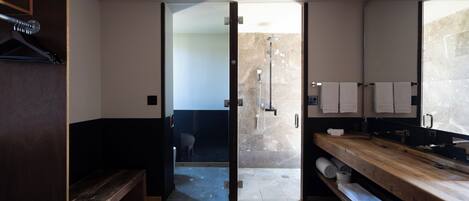 A modern bathroom with a wooden bench, a shower area, and a vanity with towels.
