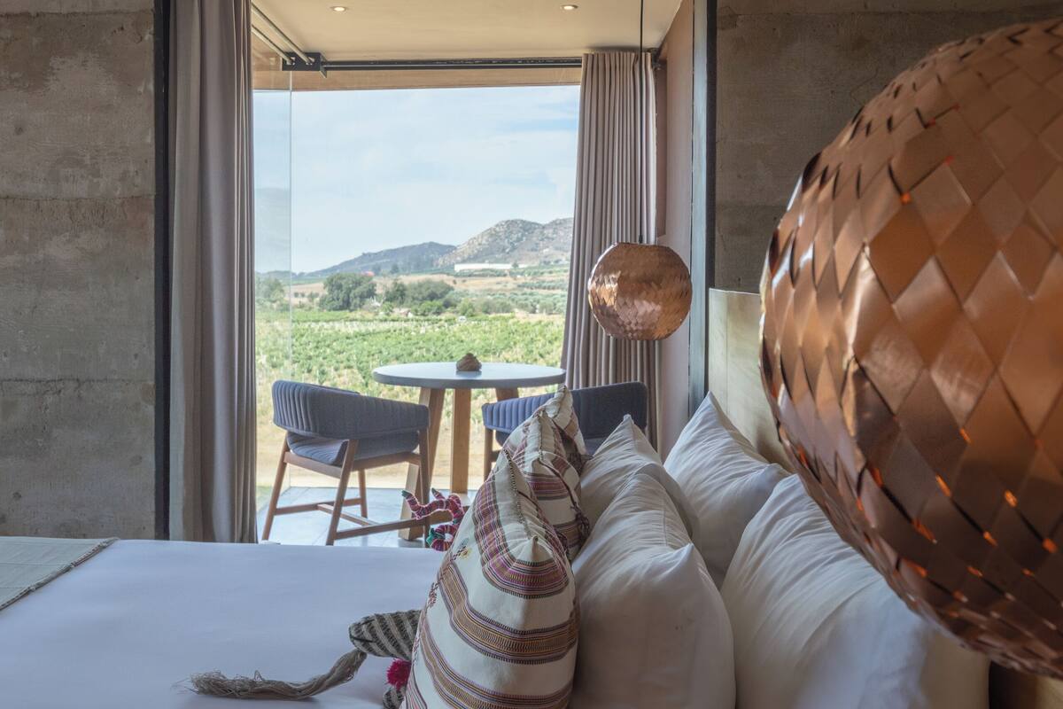 A bedroom with a large bed, a view of a vineyard, and a dining area with a table and chairs.