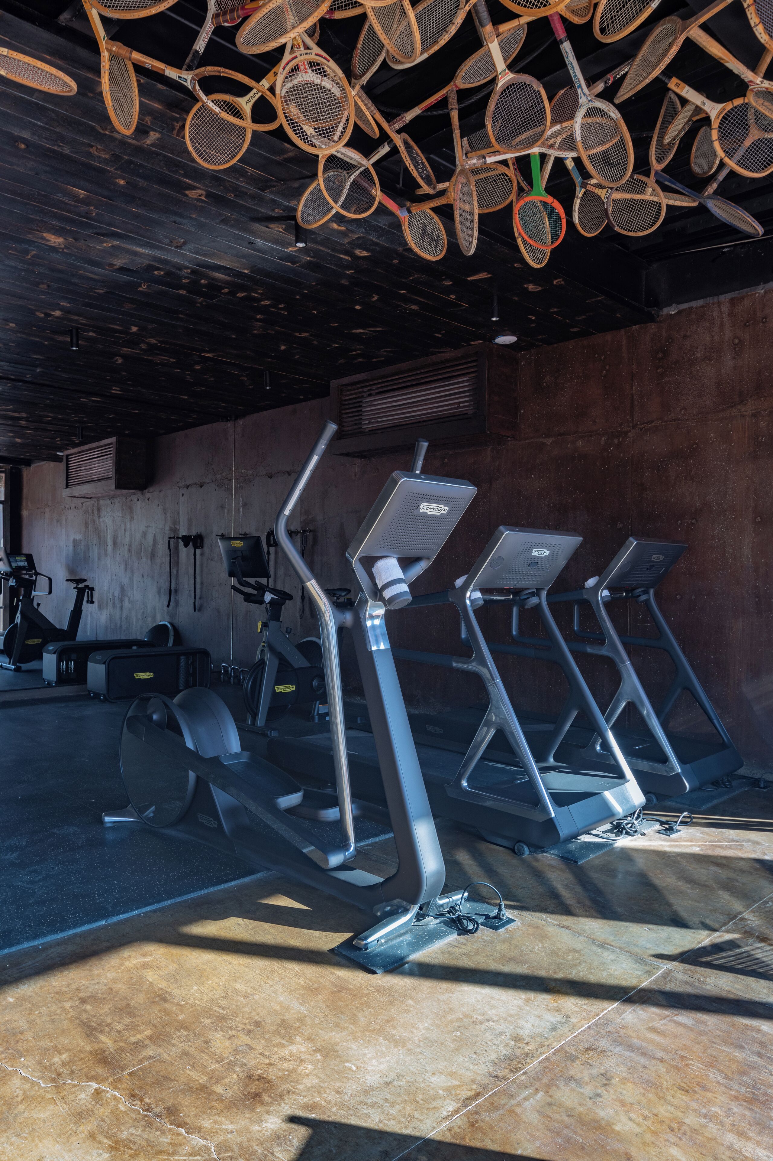 Un gimnasio con cintas de correr, bicicletas estáticas y un techo decorado con raquetas de tenis.