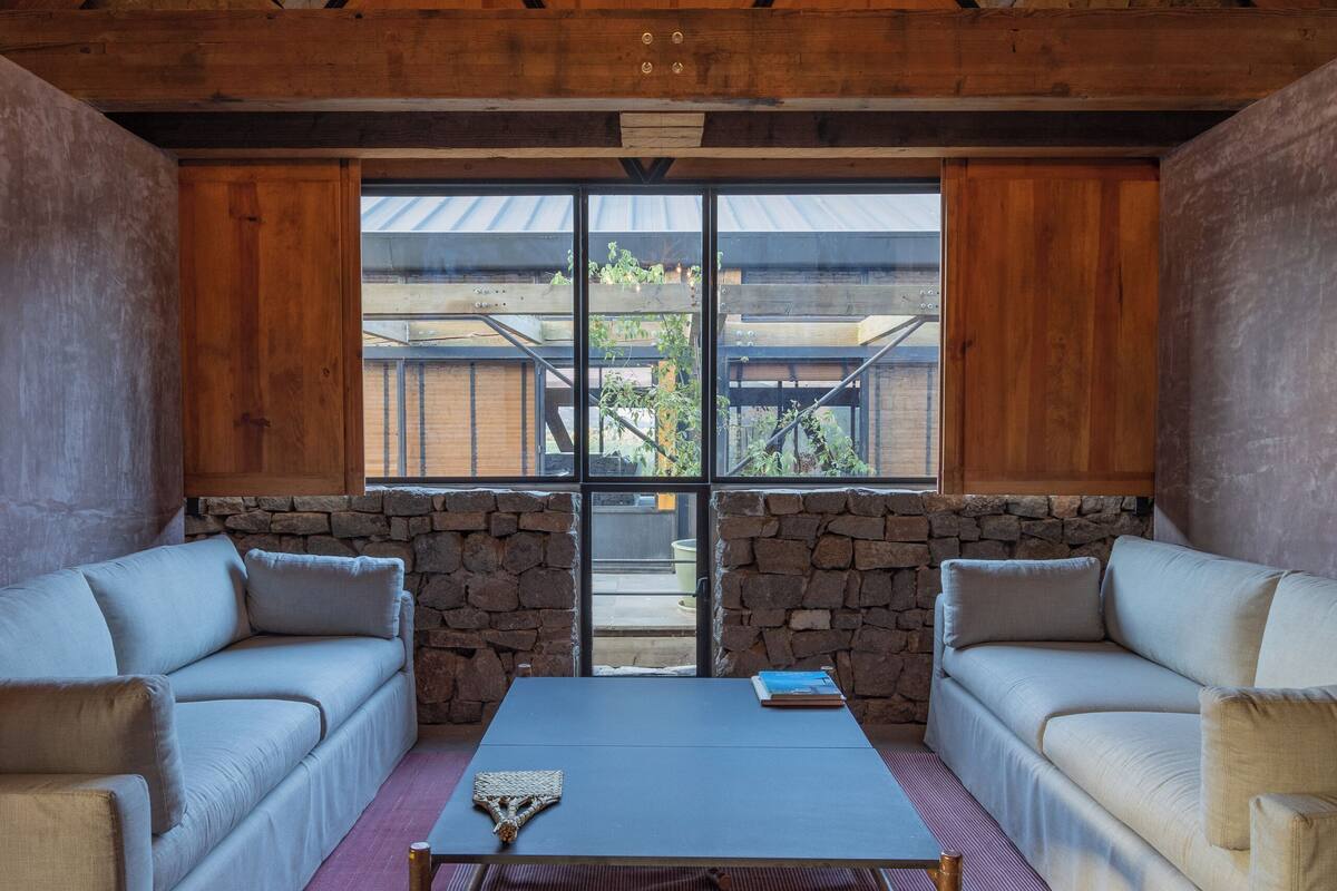 A cozy interior with a stone fireplace, wooden beams, and a large window offering a view of the outdoors.
