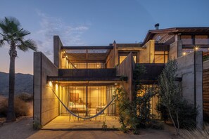 A modern house with a large open patio, a hammock, and a desert landscape in the background.