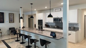 A modern kitchen with white cabinets, granite countertops, and black bar stools.