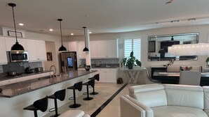 A modern kitchen with a central island, bar stools, and a seating area with white leather sofas.