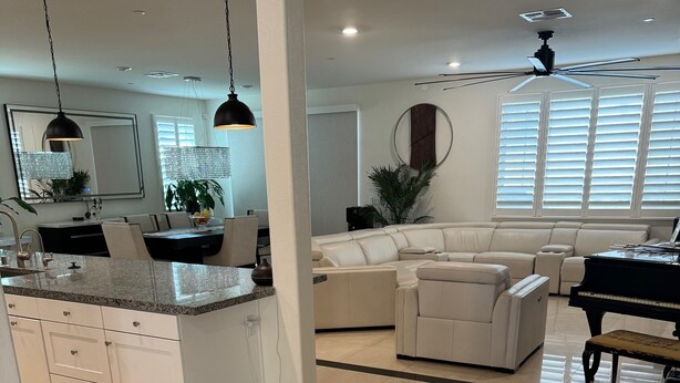 A modern living room with a sectional sofa, a piano, and a dining area with a kitchen in the background.