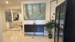 A modern kitchen with a dark-colored cabinet, a large abstract painting on the wall, and a potted plant.