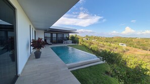 Ein modernes Haus mit Swimmingpool, einer Terrasse mit Gartenmöbeln und Blick auf die umliegende Landschaft.