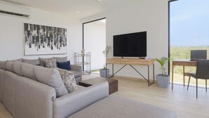 Una sala de estar moderna con un sofá gris, un televisor de pantalla plana, un escritorio de madera y una computadora portátil.