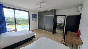 Ein Hotelzimmer mit einem großen Bett, einem Schreibtisch, einem Kleiderschrank und Blick auf einen Pool und Berge.