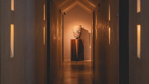 Passadís estret amb un terra de fusta i parets, que condueix a una habitació amb un objecte gran i fosc al centre.