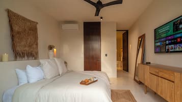 Un dormitorio con una cama, ventilador de techo, puerta de madera, televisor en la pared y un armario de madera.