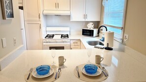 A kitchen with white cabinets, a stove, a microwave, and a sink.