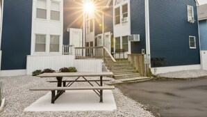 A two-story building with a front porch, a staircase, and a picnic table in front.