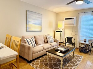 A living room with a beige sofa, a coffee table, a lamp, a small table with a basket, and a ceiling fan.