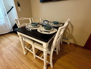 A dining table with four chairs, a black tablecloth, and blue bowls on placemats. - Sunny Beach Escape – 2BR Condo Steps from Sand •Badges • Parking (Seaside Heights)