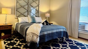 A bedroom with a bed, two bedside tables, a lamp, a decorative wall piece, and a window with curtains.