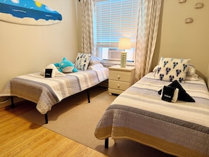A bedroom with two beds, a nightstand, a lamp, and a wall decoration. - Sunny Beach Escape – 2BR Condo Steps from Sand •Badges • Parking (Seaside Heights)