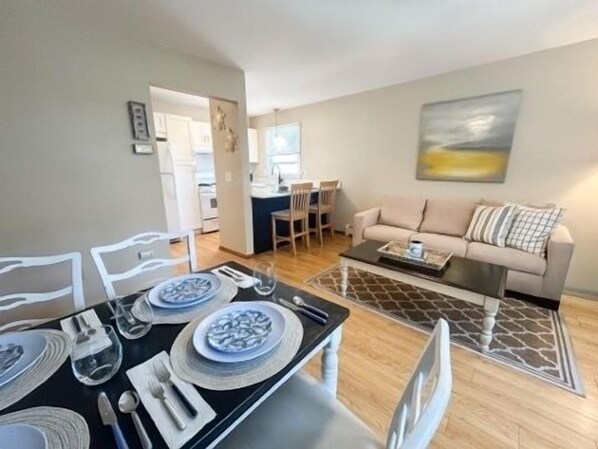 A dining area with a table set for four, a sofa, and a painting on the wall.