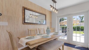 A dining area with a wooden table set for four, a large mirror above, and a view of the outdoors through glass doors.