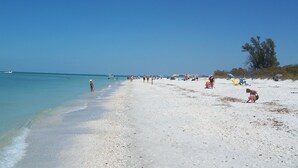 A beach with clear skies, a sandy shore, and a few people and umbrellas.