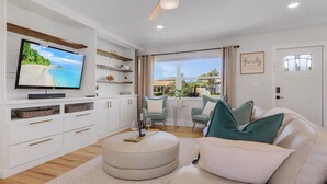A modern living room with a flat-screen TV, white furniture, and a view of the outdoors.