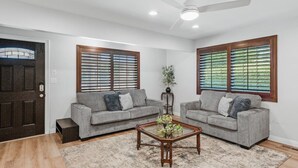 Sala de estar com dois sofás cinzas, uma mesa de centro de madeira com plantas e um ventilador de teto.