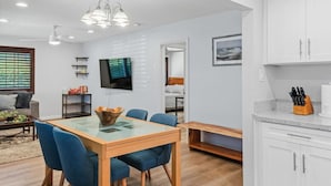Uma sala de estar moderna com área de jantar, TV fixada na parede e cozinha com armários e bancada.