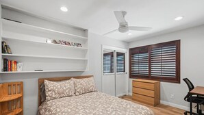 Quarto com cama, escrivaninha, cadeira, guarda-roupa e janela com persianas.