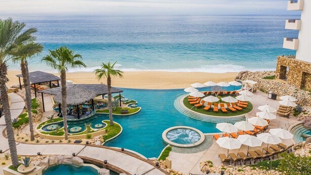 A resort with a pool area, lounge chairs, and a beach view.