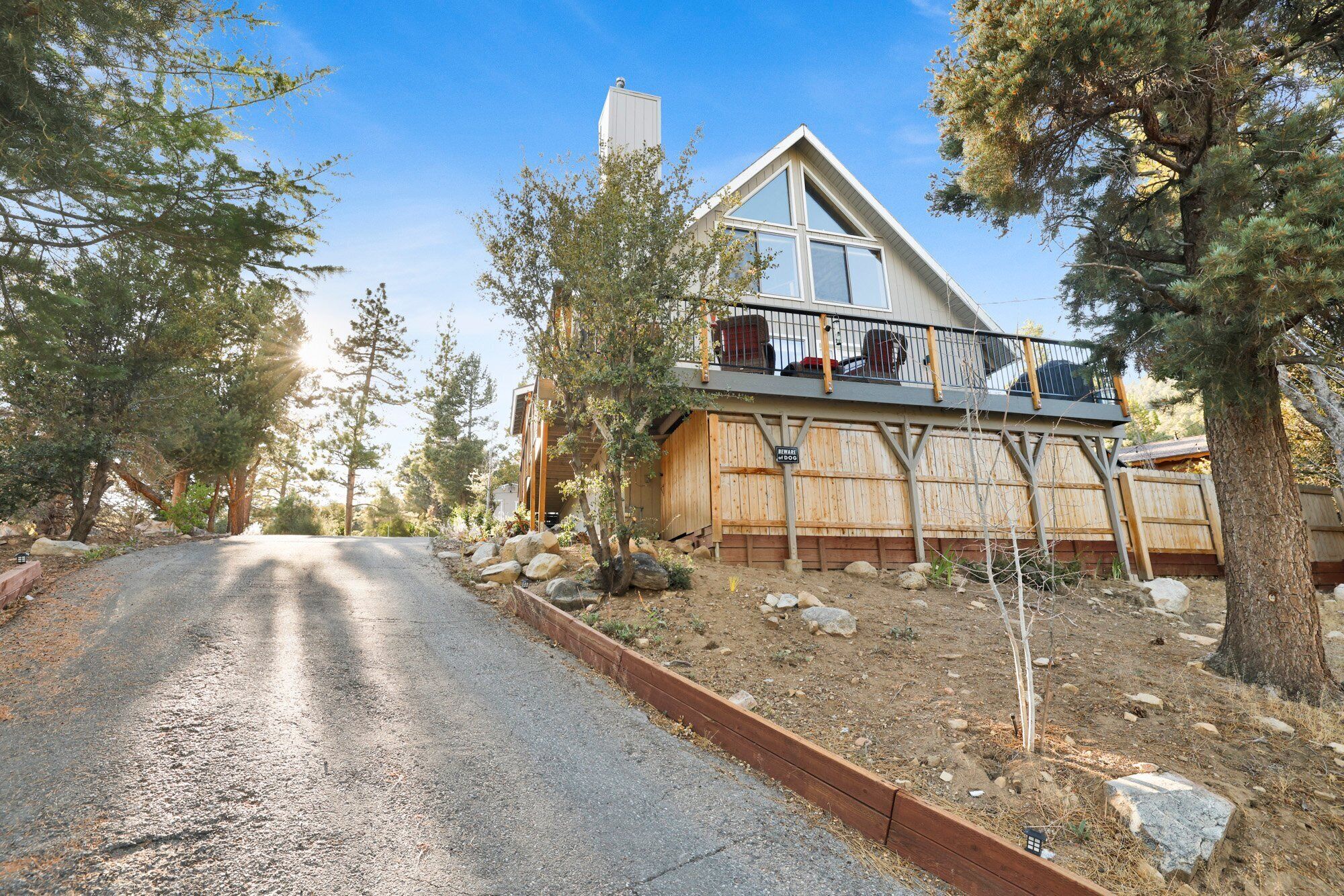 A modern house with a large balcony, surrounded by trees and a gravel driveway.