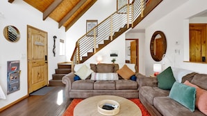 A spacious living room with a wooden staircase, a brown sofa set, and a round coffee table. - Chimney Peak Chalet#2048 (Big Bear City)